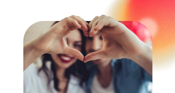 A couple smiles, forming a heart together with their hands.