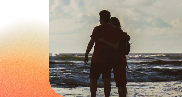 An image of a couple on the beach. They are visible in silhouette, with the ocean in front of them.