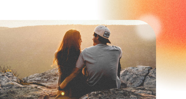 An image of a couple sitting on the beach looking out at the ocean and the sunset.