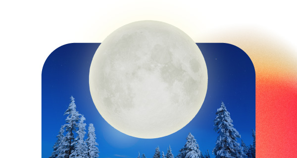 An image of a large Full Moon over a dark blue background. Snowy trees line the background.