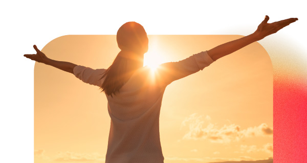 A woman with her arms spread out to the sun, which is setting in the distance.