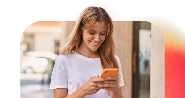 A woman with blonde hair and a white shirt, smiling down at her phone.